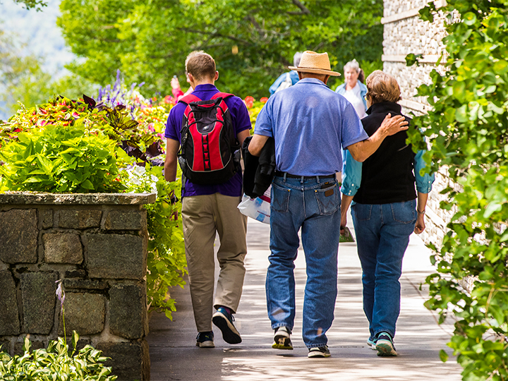Un couple de personnes âgées et un jeune homme visitent l'ADKX et marchent sur un chemin où fleurissent de magnifiques fleurs.