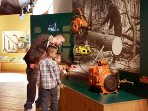 A father and his two sons looking at saws in the Work in the Woods: Logging in the Adirondacks exhibit.