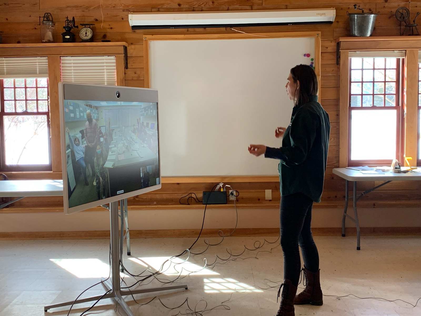 Una educadora de ADKX se encuentra frente a una pizarra inteligente que la conecta virtualmente con un aula.