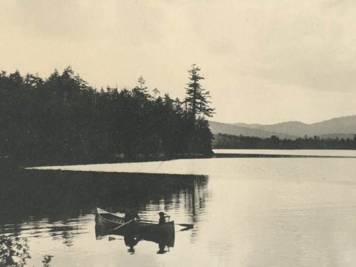 A vintage image of a canoe out on Blue Mountain Lake. Learn about the history of the museum and of the Adirondacks at the ADKX.