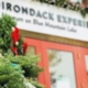 Cropped view of the sign about the entrance of the Adirondack Experience, decorated with wreaths and evergreen garland for the holidays.