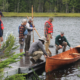 A group of people are standing on a dock, looking at a guideboat.