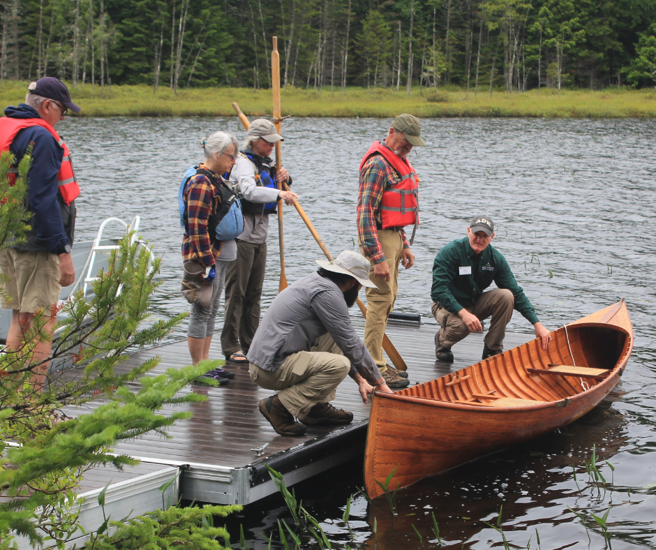A group of people are standing on a dock, looking at a guideboat.