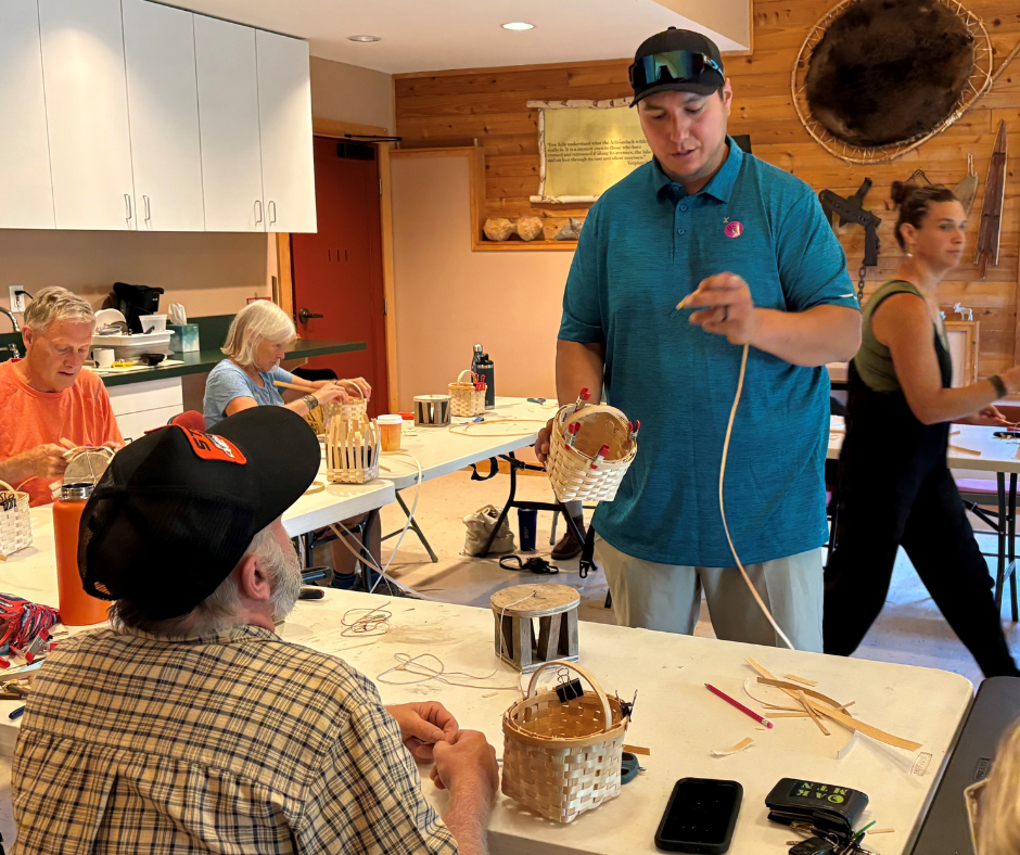 A man in a blue shirt is showing a person how to make a basket.