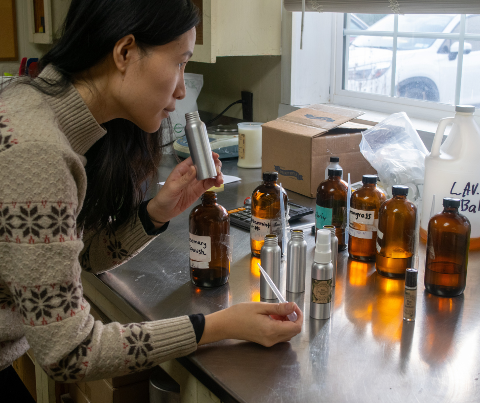 A woman is standing at a counter with several bottles of oils in front of her.