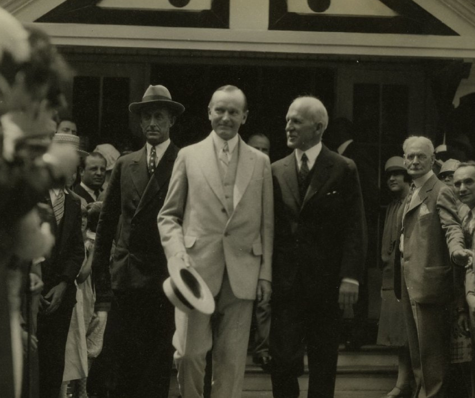 Two men in suits and hats are standing in front of a crowd of people.