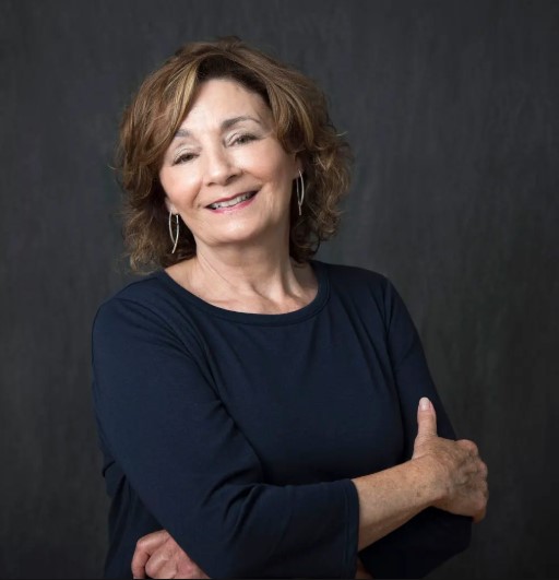 A woman wearing a black shirt and earrings is smiling for the camera.