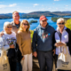 A group of five people are standing on a deck overlooking Blue Mountain Lake. They are posing for a picture and smiling.