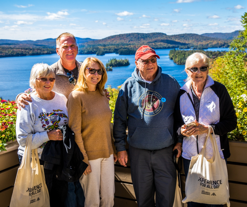 A group of five people are standing on a deck overlooking Blue Mountain Lake. They are posing for a picture and smiling.