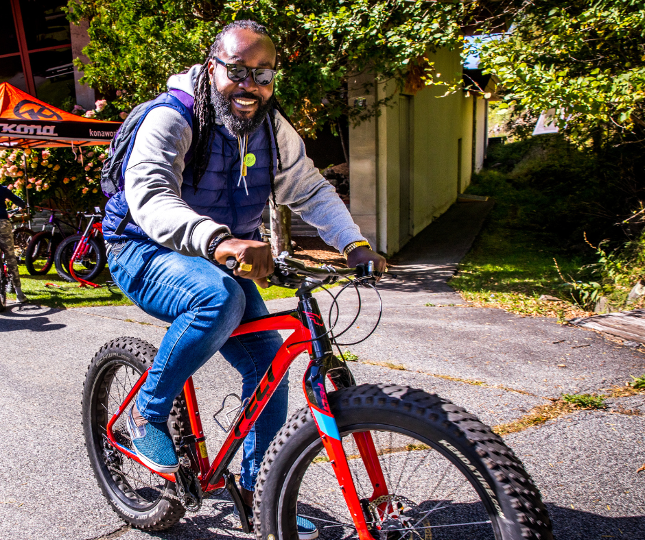 A man wearing a black vest is riding a bicycle on a sidewalk.