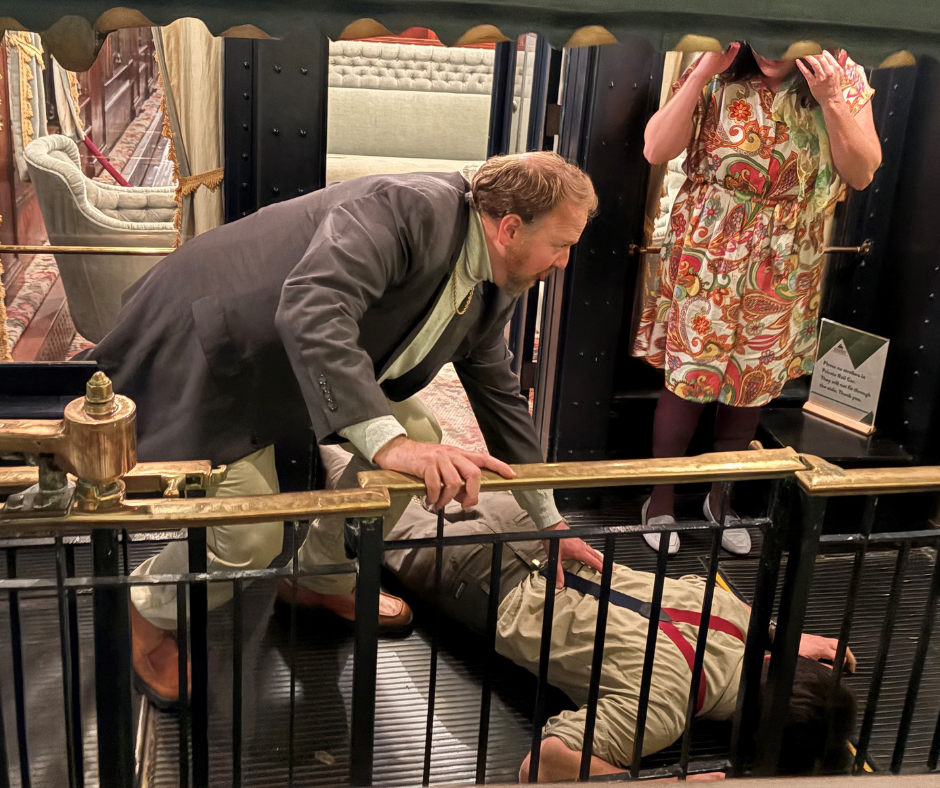 A man is lying on the floor while another man is bending over him. A woman is standing nearby.