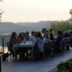 A group of people are sitting around a table on a deck, enjoying a meal together.