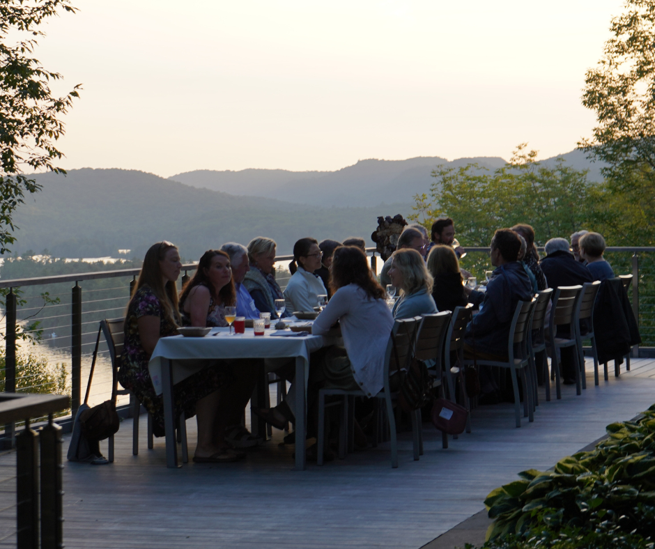 A group of people are sitting around a table on a deck, enjoying a meal together.